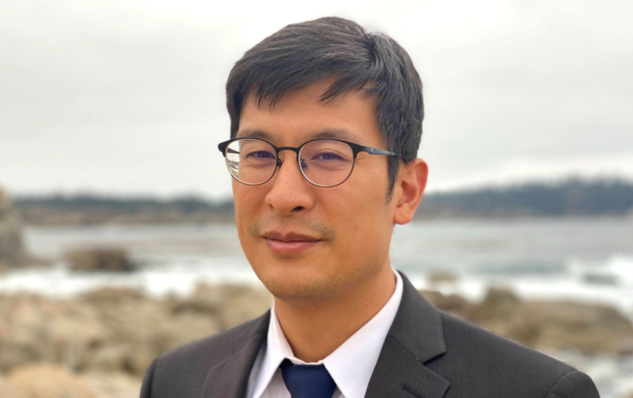 Headshot image of Columbia Professor James Chu in a suit, outdoors on a beach.