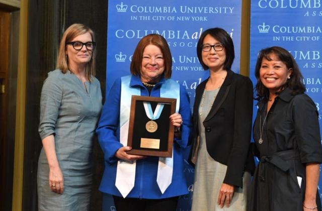 Four smiling alumnae with one in regalia holding a 2022 CAA Alumni Medal after medalist ceremony